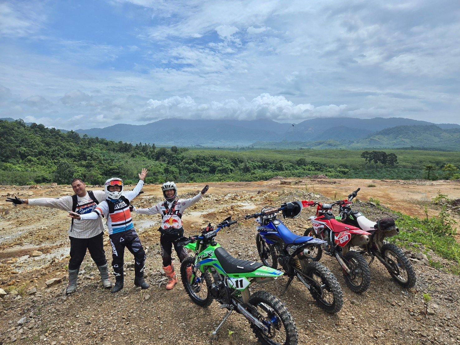 Happy dirt bike tour group posing with their bikes against dramatic mountain ridges in Krabi
