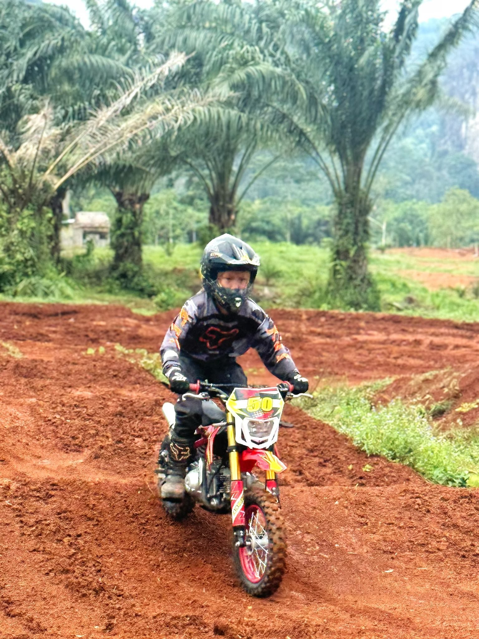 Young rider practicing on a red dirt motocross track with a mini dirt bike in Krabi