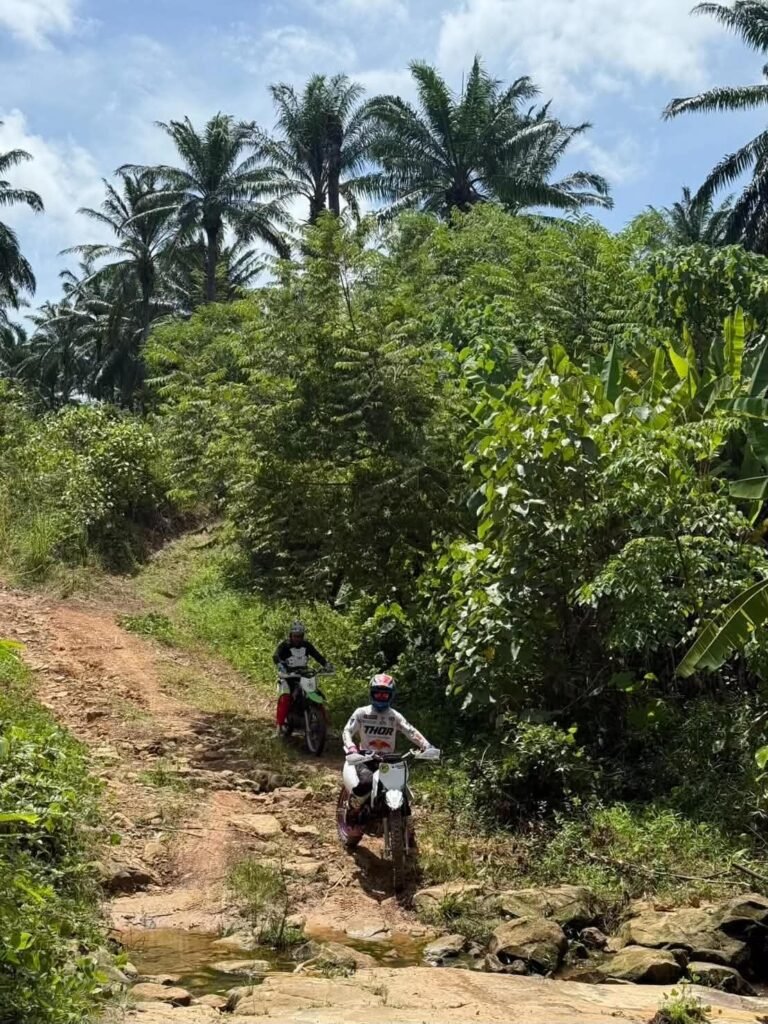Motocross riders cruising along a dirt trail through tropical banana and palm trees in Krabi