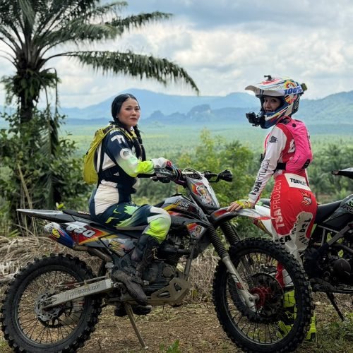 Two female motocross riders posing with dirt bikes overlooking Krabi mountain landscape