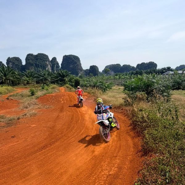 Motocross dirt bikes riding through red dirt trail with limestone mountain backdrop