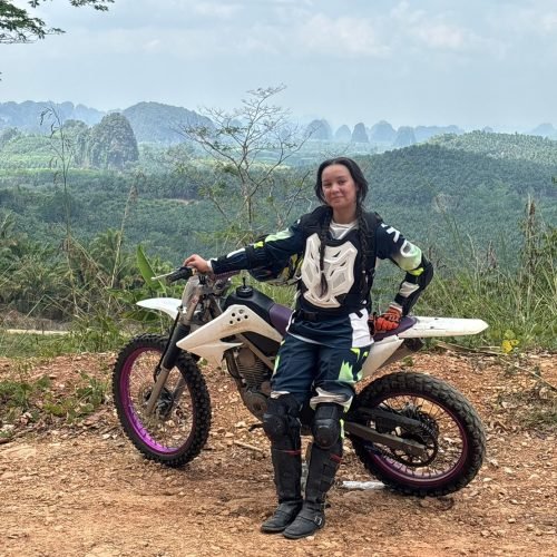 Female adventure rider standing with dirt bike overlooking iconic Krabi mountain scenery